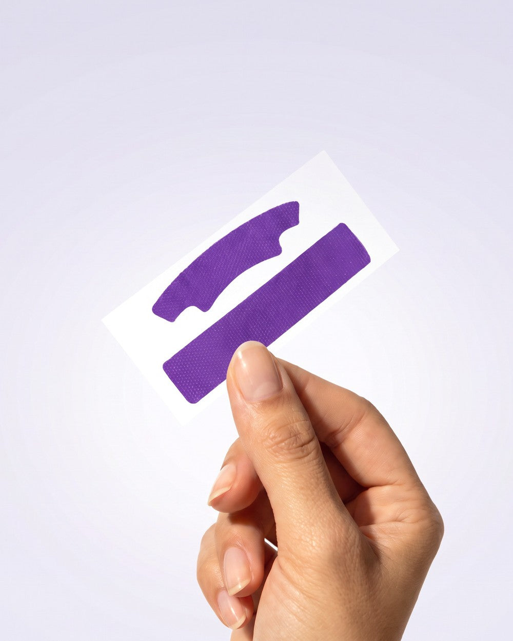 Mano sosteniendo un par de tiras blanqueadoras PURPLE STRIPS moradas